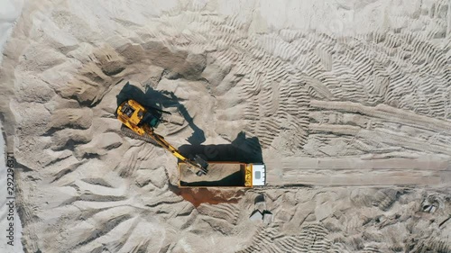 Aerial view of bulldozer loading sand into empty dump truck in open air quarry.