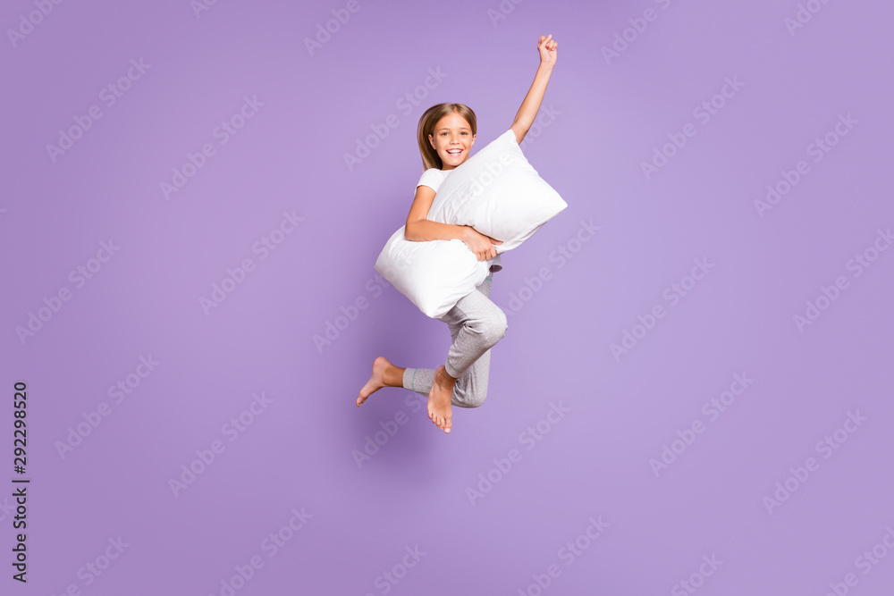 Full length photo of positive cheerful funny kid jump raise fist ahead imagine she strong superhero fly with pillow wear white comfort t-shirt pants barefoot isolated violet purple color background