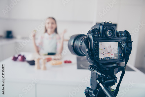 Close-up view of professional cam recording video lesson attractive beautiful cheerful cheery pre-teen girl making useful vitamin vegs salad dish in light white interior kitchen house indoors