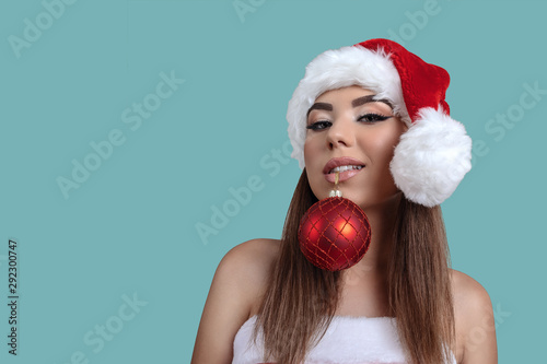 Beautiful Girl in Santa Claus hat holds Christmas ball with teeth