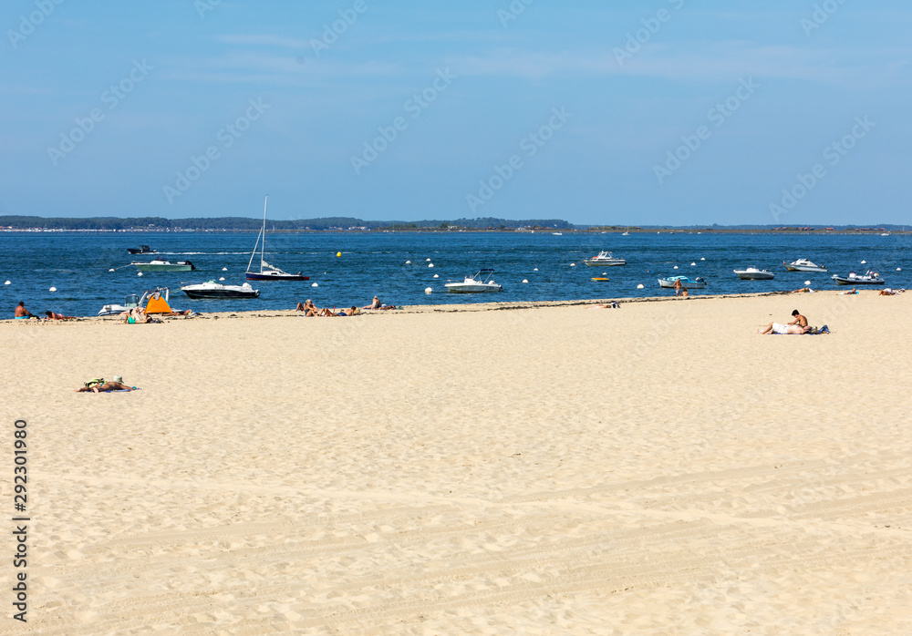 People are enjoying a sunny day on a sandy beach in Arcachon, France