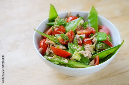 snow peas and cherry tomatoes with tuna as a healthy salad for low carb diet in a white bowl on a wooden table, copy space