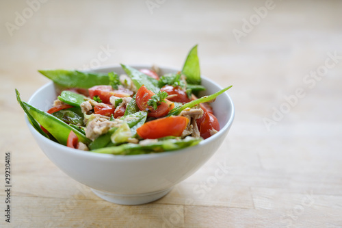 healthy salad of snow peas and cherry tomatoes with tuna in a white bowl on a wooden table, copy space, selected focus, narrow depth of field