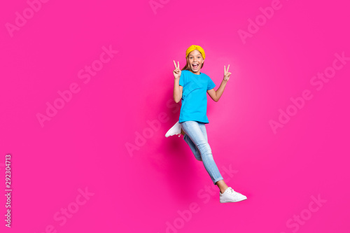Full body photo of funny funky rejoicing blonde haired kid have fun jump run after discounts make v-signs wear denim jeans blue yellow outfit sneakers isolated over pink color background