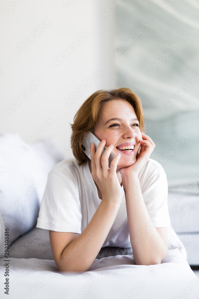 Happy young woman lying on the couch at home, talking on the phone with friend Happy young woman lying on the couch at home, talking on the phone with friend