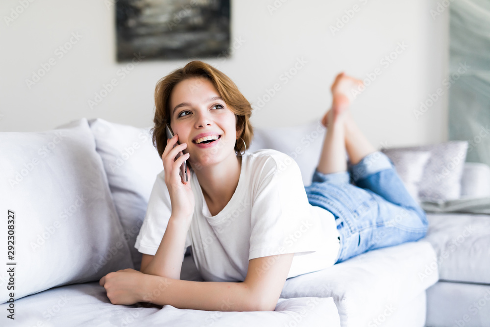 Happy young woman lying on the couch at home, talking on the phone with friend Happy young woman lying on the couch at home, talking on the phone with friend