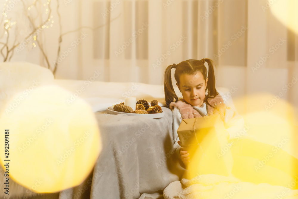 Happy little girl sitting by a fireplace in a cozy dark living room on Christmas eve Happy little girl sitting by a fireplace in a cozy dark living room on Christmas eve