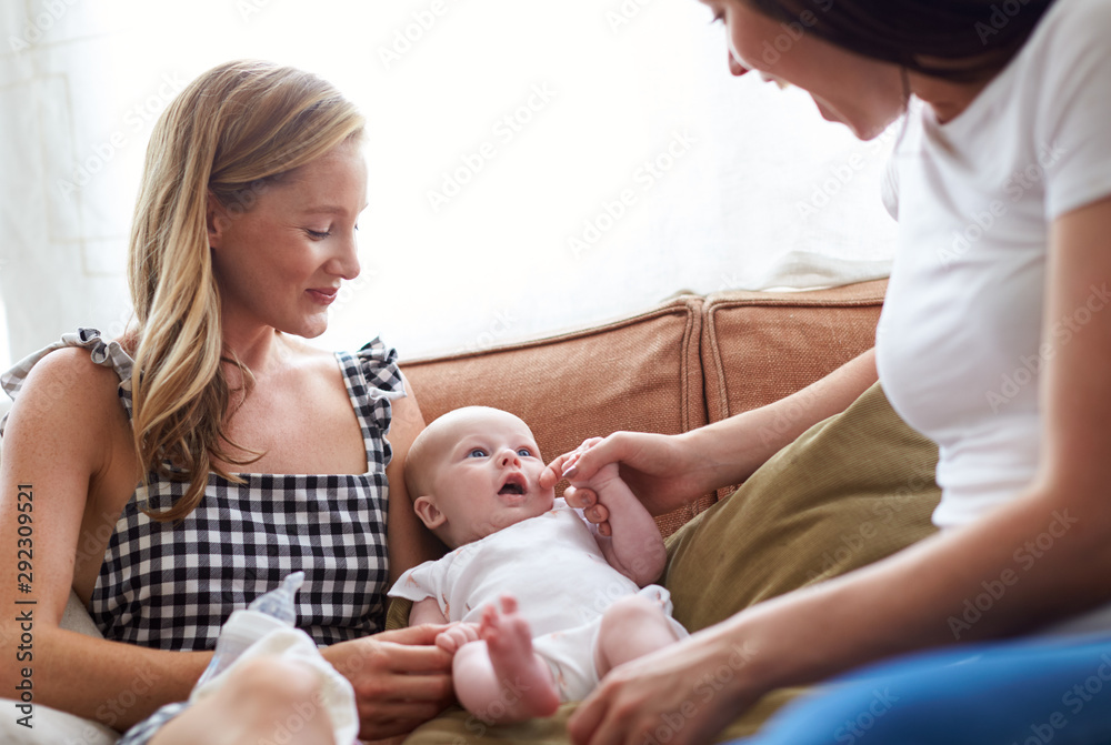 Obraz premium Loving Female Same Sex Couple Cuddling Baby Daughter On Sofa At Home Together