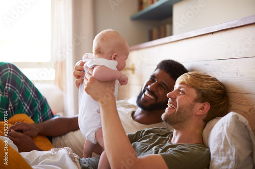 Loving Male Same Sex Couple Cuddling Baby Daughter In Bedroom At Home Together photo