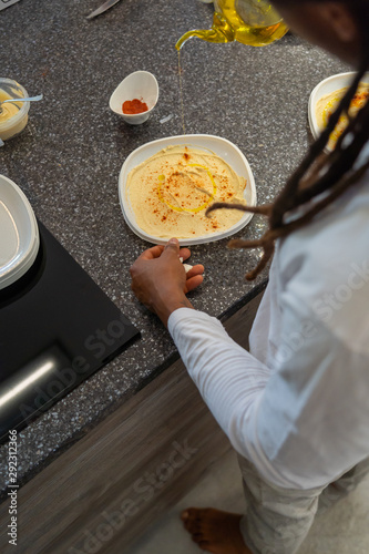 Young African-American With Dreadlocks In The Hair. He is preparing hummus in a modern kitchen.
