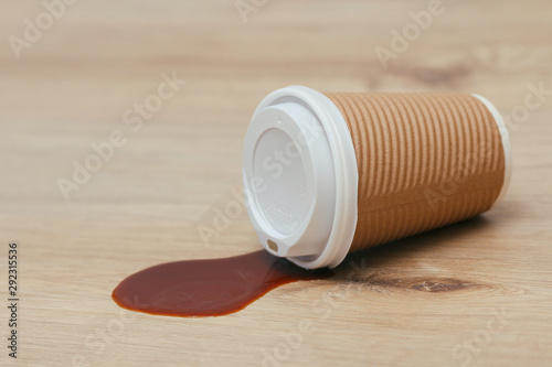 Spilled liquid on the floor. Paper coffee cup with plastic lid. Garbage. Sticky surface. Need cleaning.