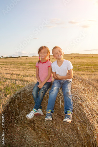 happy children sitting on haystack at sunset. kids, girl with boy sitting in field