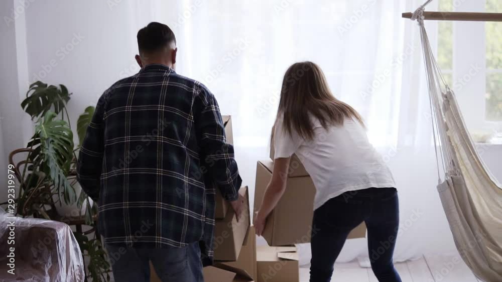 A young couple moving into a new home. A couple is carrying boxes and putting then on the floor. Beautiful couple are exciting about the apartment. The girl jumping to the arms of boyfriend A young couple moving into a new home. A couple is carrying boxes and putting then on the floor. Beautiful couple are exciting about the apartment. The girl jumping to the arms of boyfriend
