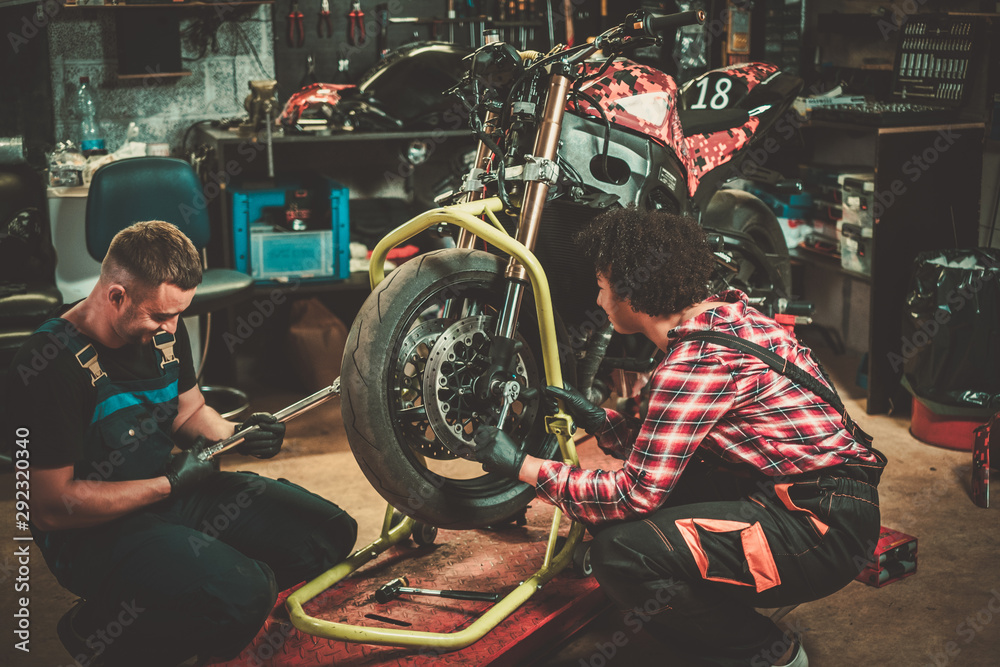 Mechanic and his helper repairing a motorcycle in a workshop