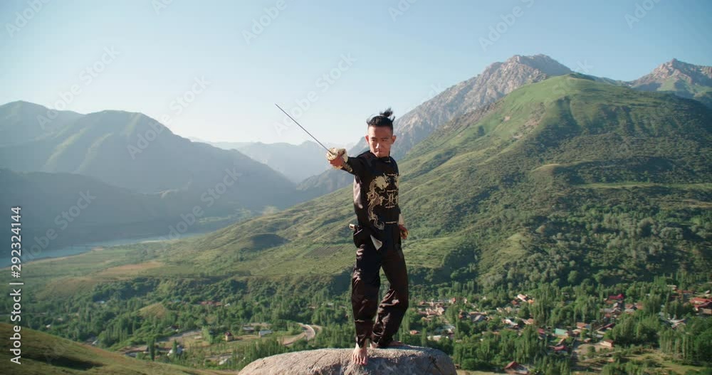 Young man practicing kung fu with sword. Tai Chi at the top of the mountain. Sword of the Shaolin monk. 4K Slow motion.