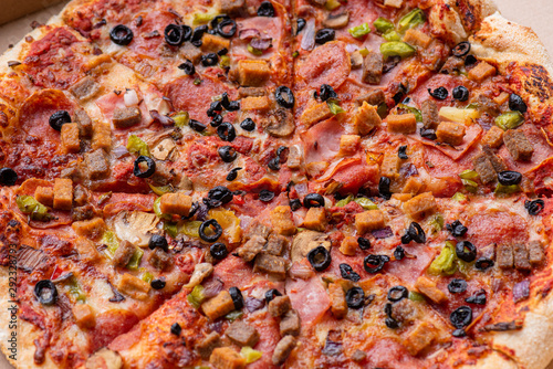 Delicious Italian pizza with bacon, olives, sausages and mushrooms. Top view. Fresh tasty pizza in cardboard box - close-up.