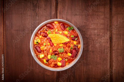 Chili con carne, overhead shot on a dark rustic wooden background with a nacho chip