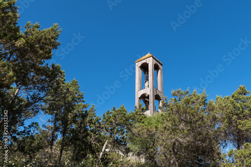 Wooden bell tower framed by tree branches against a blue sky photo