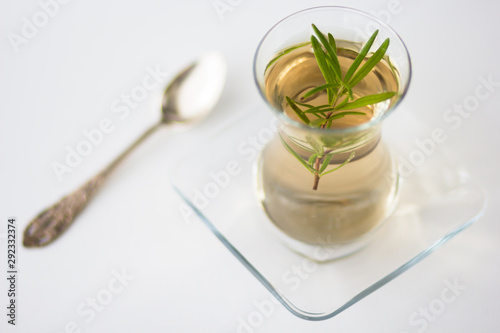 Rosemary tea in Armudu glass with branch of rosemary in it and spoon on the table on white background