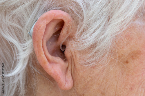 Hearing aid. Female pensioner with white hair wearing a Behind The Ear, BTE, hearing aid. Close up of ear.