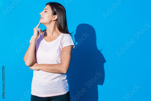 Beautiful cheerful young girl wearing casual clothes standing isolated over blue background on a sunny day. Woman feels dreamy. People and emotions image concept with copy space.