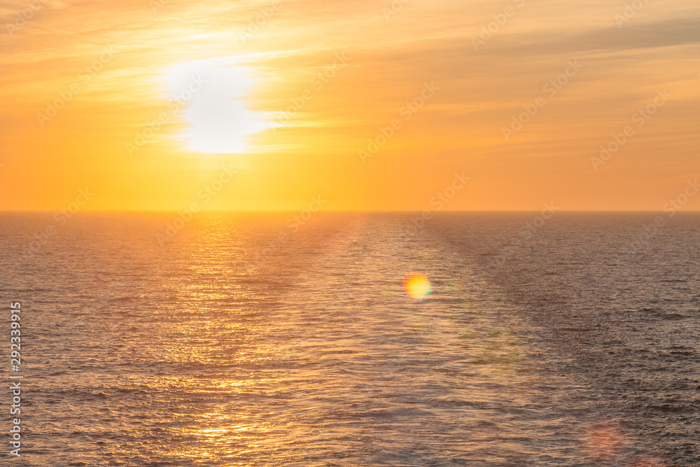 Sun about to set on the sea where you can see the wake left by a cruise ship