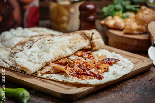 Chicken kebab doner with ketchup inside of flatbread on wooden board