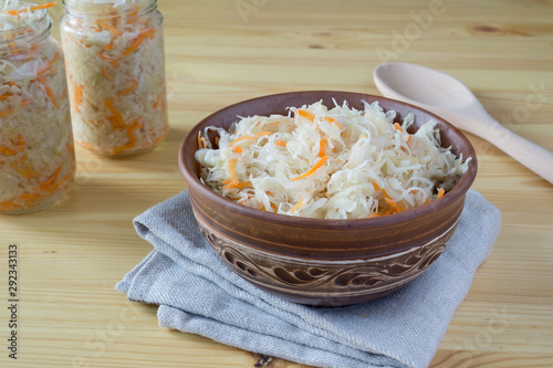 Sour cabbage fermented sauerkraut with carrot in a bowl and glass jar. Marinated cabbage on wooden background