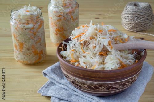Sour cabbage fermented sauerkraut with carrot in a bowl and glass jar. Marinated cabbage in wood spoon on wooden background