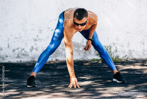 Fototapeta Naklejka Na Ścianę i Meble -  Muscular young man stretching before exercises outdoors against concrete wall. Athlete male stretches after workout outside. Sport and people concept. Copy space for your text