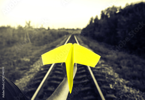 Guy is holding yellow handmade paper plane on black and white background. Freedom concept photo with rail tracks. Travel lifestyle motivation. Railway transport industry.