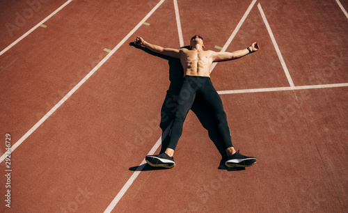 Top view image of young athlete man lying on racetrack at stadium taking rest. Professional shirtless sportsman resting after training session. People, sport and healthy lifestyle