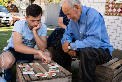 Conceived young man in grey t-shirt playing cards on a wooden box with old grandfather in blue shirt
