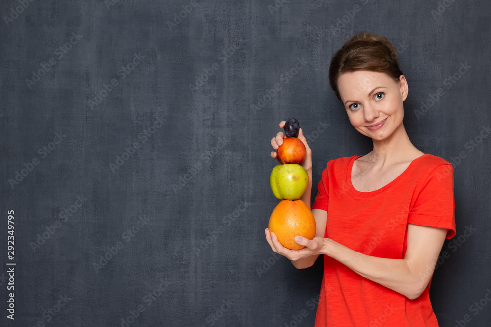 Portrait of happy woman making pyramid from different fruits Portrait of happy woman making pyramid from different fruits