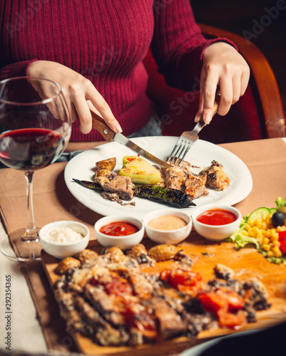 Woman cutting grilled chicken steak served with grilled peppers, salad and wine