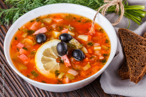 Traditional Russian meat soup Solyanka in bowl on rustic wooden table