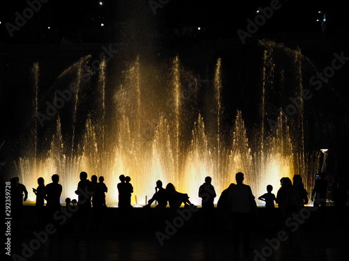 Silhouette of people watching at colorful illuminated musical fountains in the evening. Light and water night show performance.