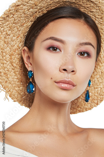 Cropped portrait shot of a young Asian girl in a straw hat and white striped shirt wearing stud earrings with blue drop-shaped pendants made of gems similar to sapphire. photo