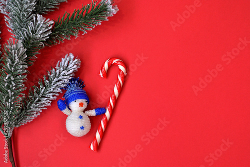 Christmas tree little toy snowman with crochet striped candy lollipop on the red background top view. Imitative fir-tree as a symbol of new year and winter holidays card picture. Flat lay card photo