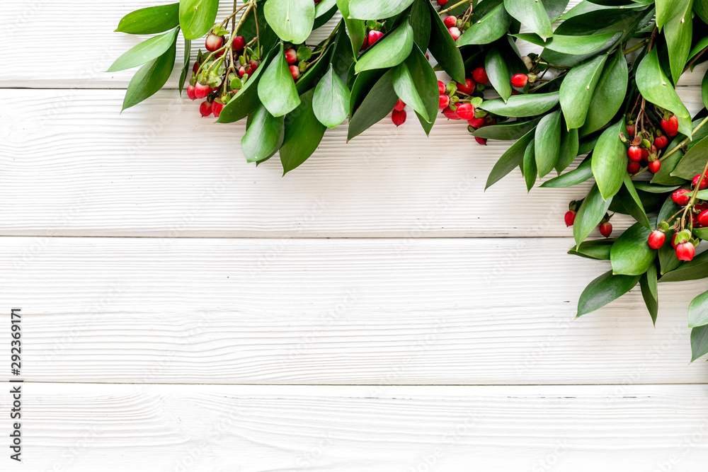 Green leaves and red berries frame on white wooden background top view copyspace Green leaves and red berries frame on white wooden background top view copyspace