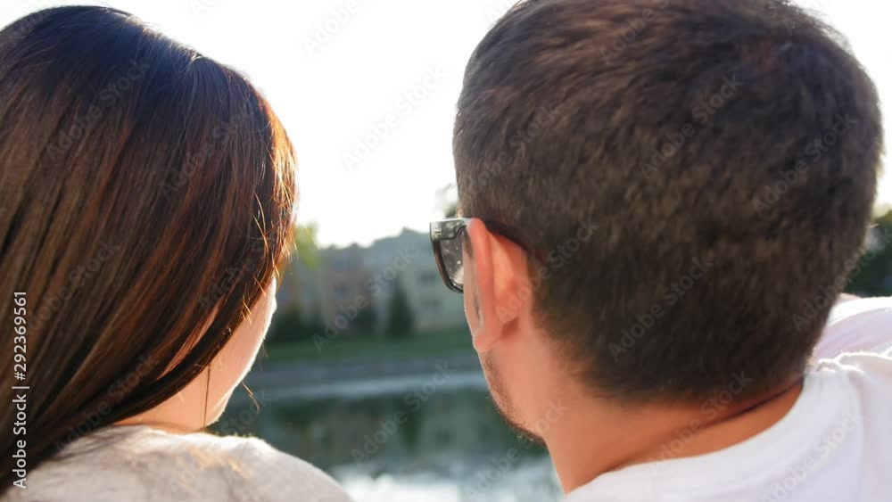 Romantic couple talking and sitting on the green grass near the pond on sunset. Back view. Couple Trust, Love and Happiness concept. Close up shot. Romantic couple talking and sitting on the green grass near the pond on sunset. Back view. Couple Trust, Love and Happiness concept. Close up shot.