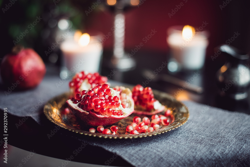 Still life composition with juicy red cut cleared pomegranate on a copper plate, burning candles and other oriental decor on the black table. Soft selective focus. Copy space. Still life composition with juicy red cut cleared pomegranate on a copper plate, burning candles and other oriental decor on the black table. Soft selective focus. Copy space.