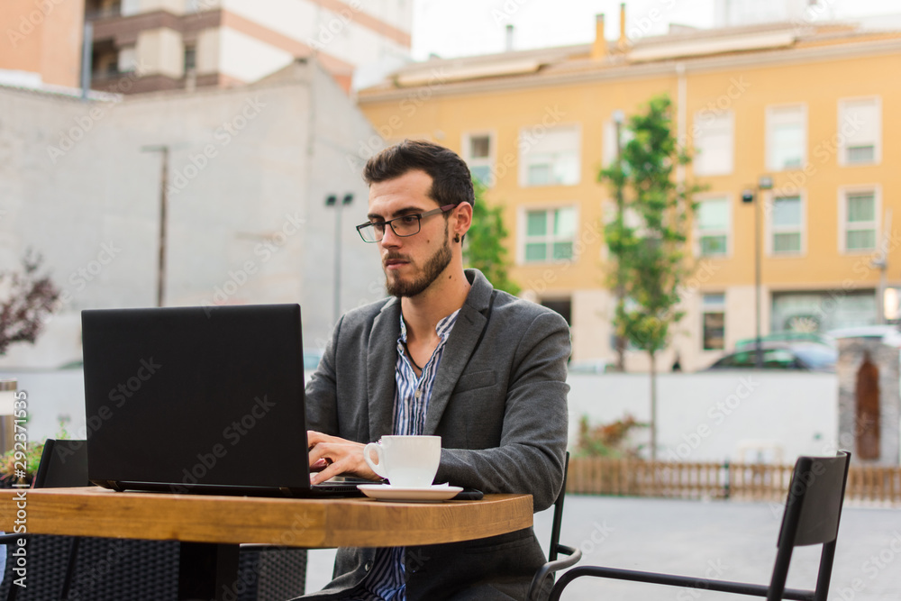 Young businessman is working in a bar terrace with his laptop and smartphone Young businessman is working in a bar terrace with his laptop and smartphone