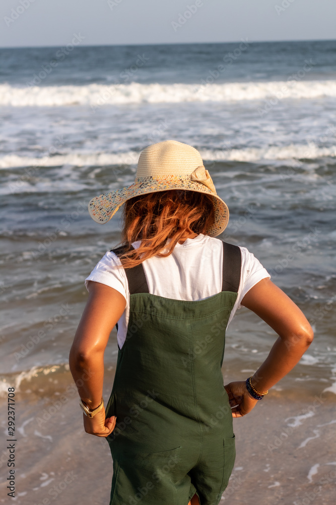 Rear view of a young African lady in a hat facing the ocean