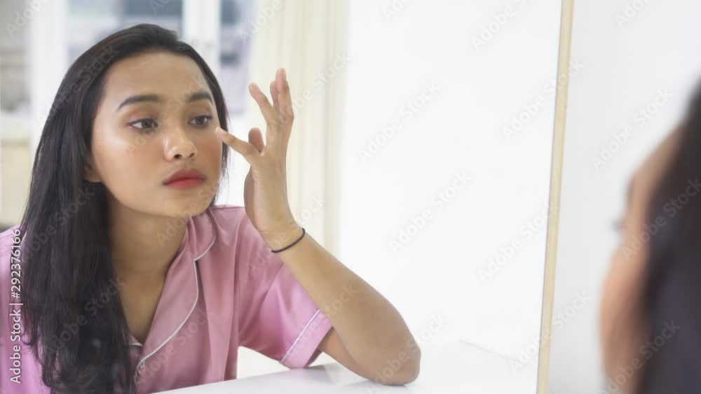 Pretty teenage girl touching face and looking at mirror in the bedroom ...