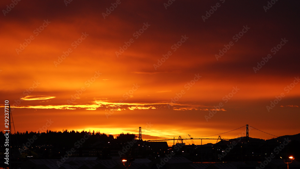Red sky at night. Silhoutte view of North Vancouver Shipyards and LionsGate Bridge against fiery sunset