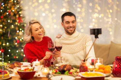 christmas, holidays, technology and people concept - happy couple in taking selfie by smartphone at home dinner