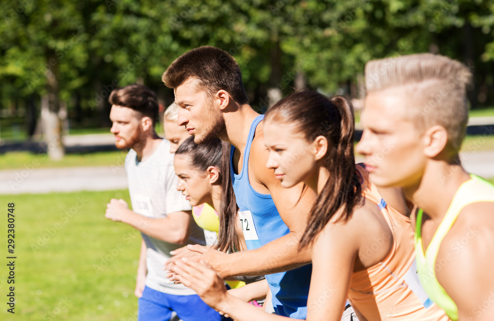 fitness, sport, race and healthy lifestyle concept - group of people or sportsmen with badge numbers on start of running marathon at summer park fitness, sport, race and healthy lifestyle concept - group of people or sportsmen with badge numbers on start of running marathon at summer park