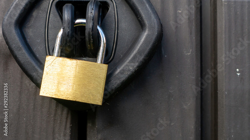 Close up of a chrome and gold textured padlock locking a plastic outside storage unit. Image taken on an overcast day.