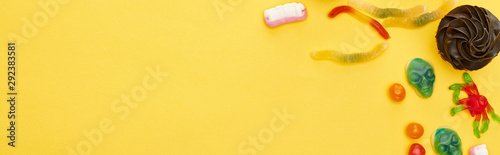 Fototapeta Naklejka Na Ścianę i Meble -  panoramic shot of colorful gummy sweets and cupcake on yellow background, Halloween treat